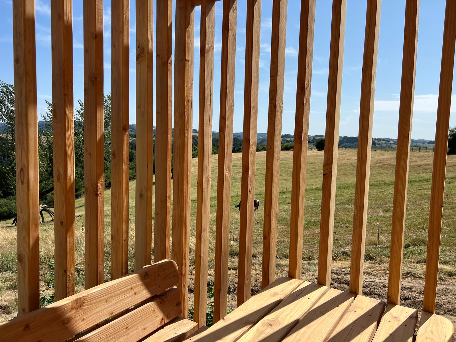 Détail claustra bois de la terrasse COQhome ouvert sur la campagne et un cheval au loin