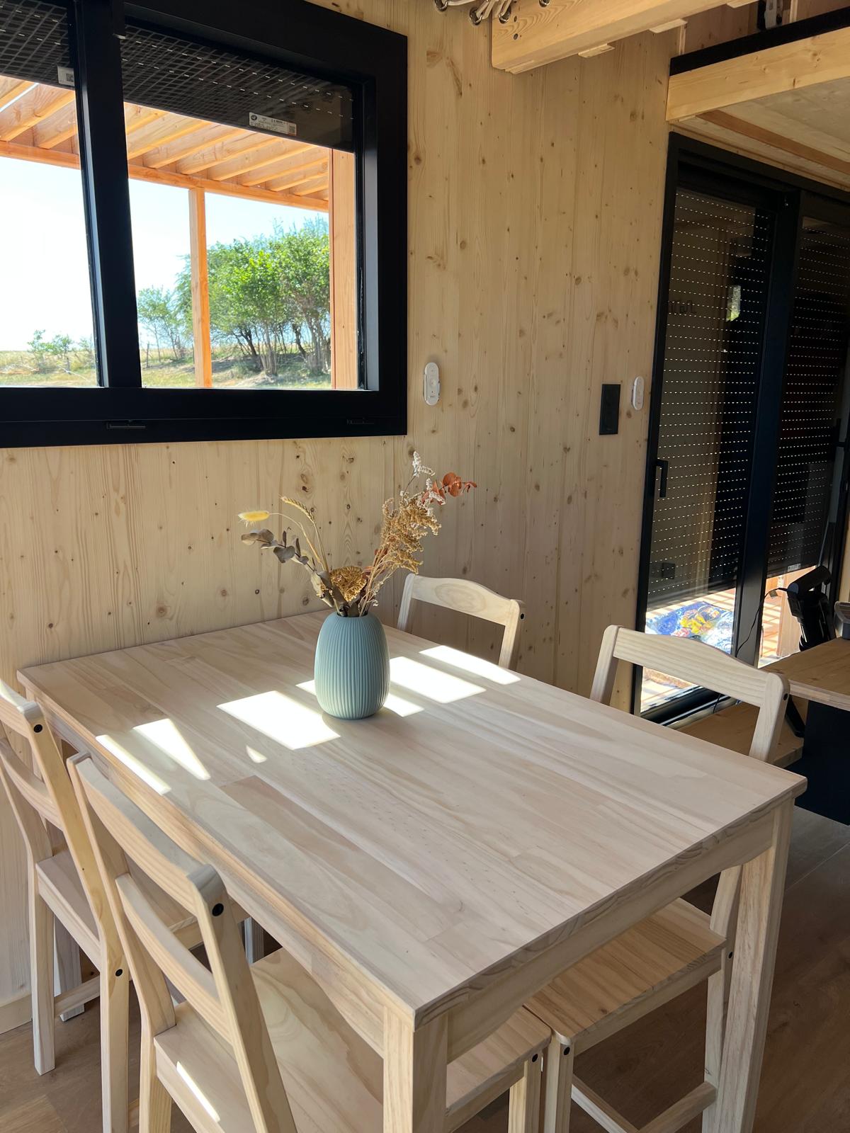 Table à manger en bois clair avec vase et bouquet séché, lumière naturelle